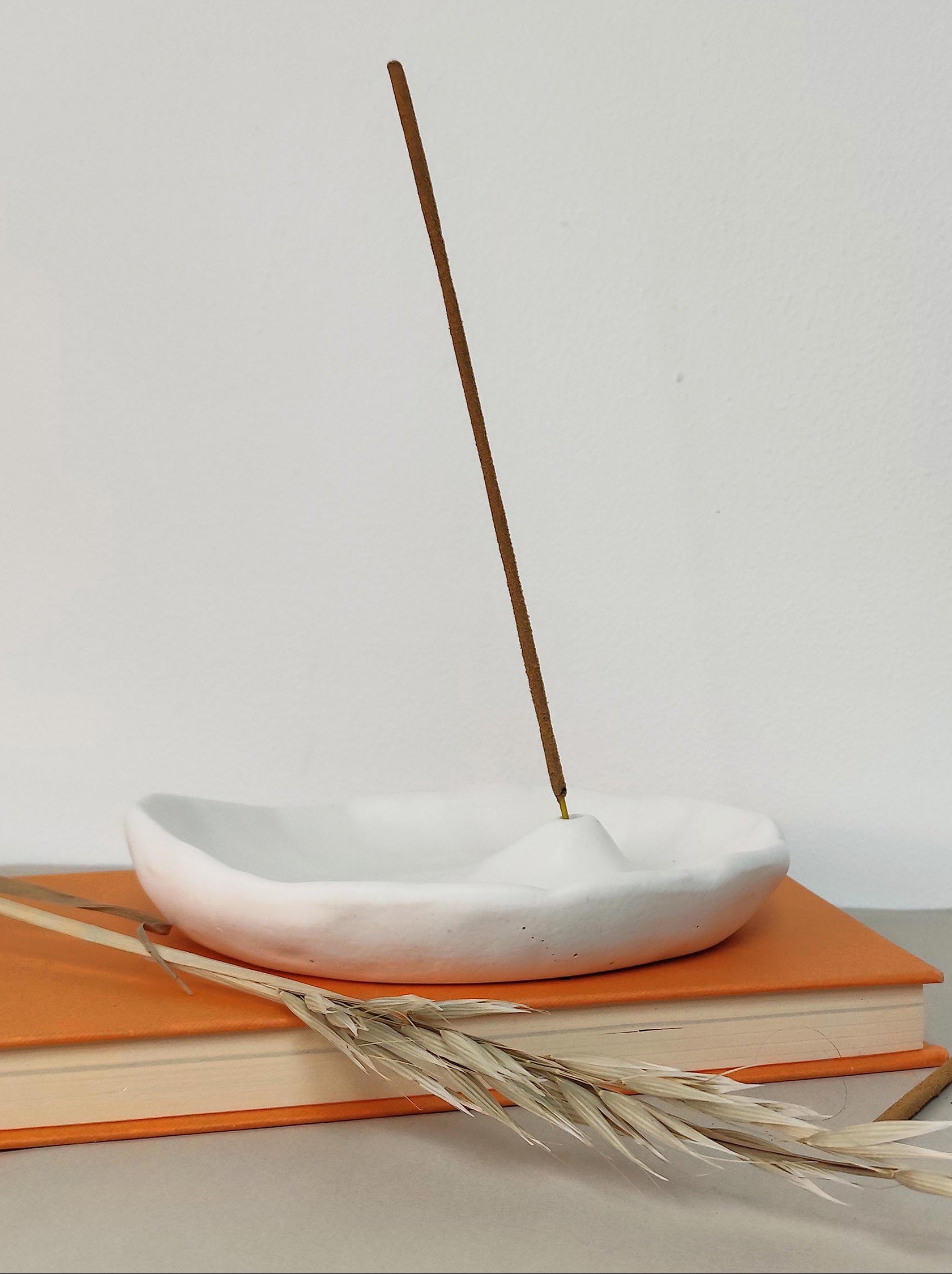 Incense stick burning in a white jesmonite holder on orange books with a white minimal background