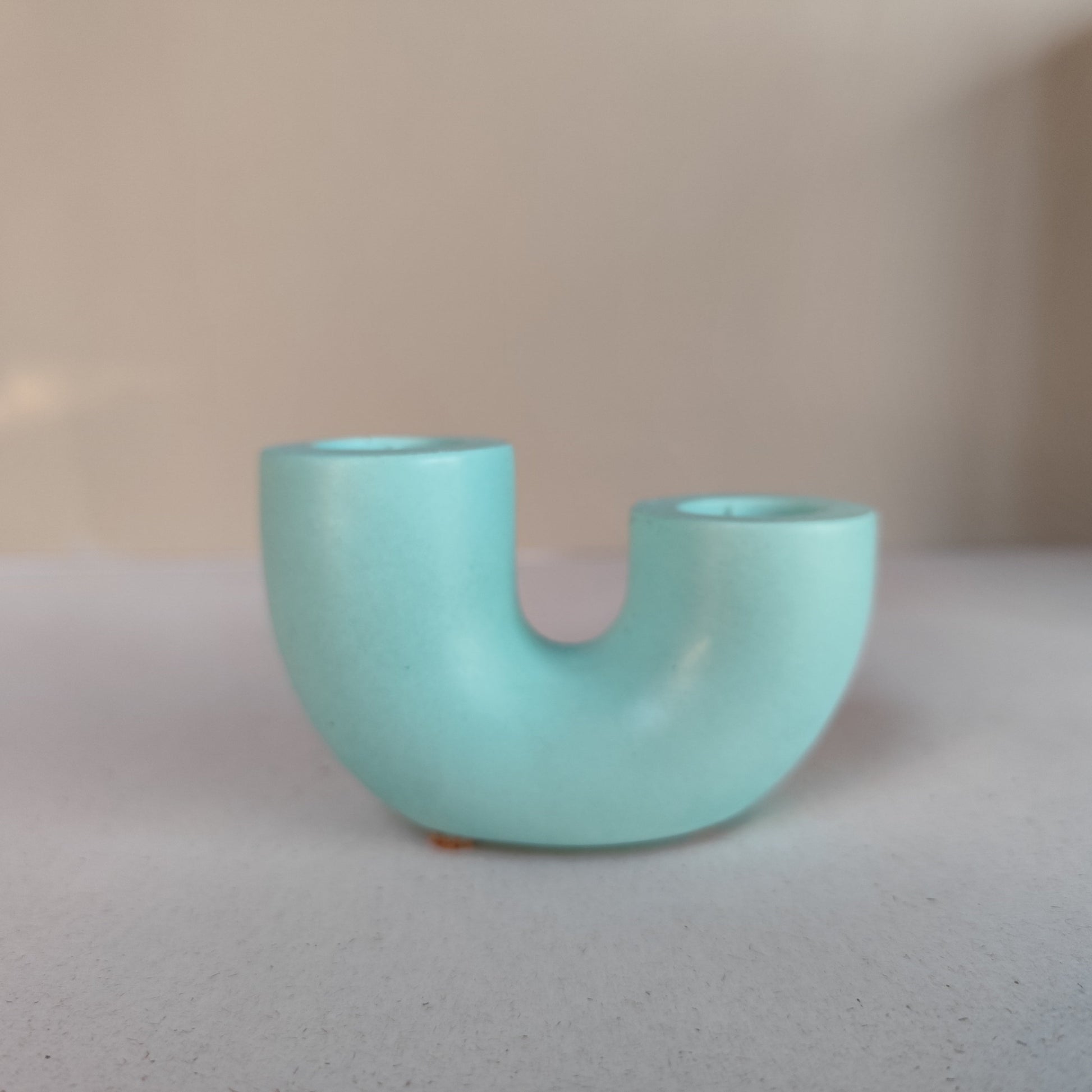A dual U-shaped candle holder in a mint, green color, placed on a neutral background