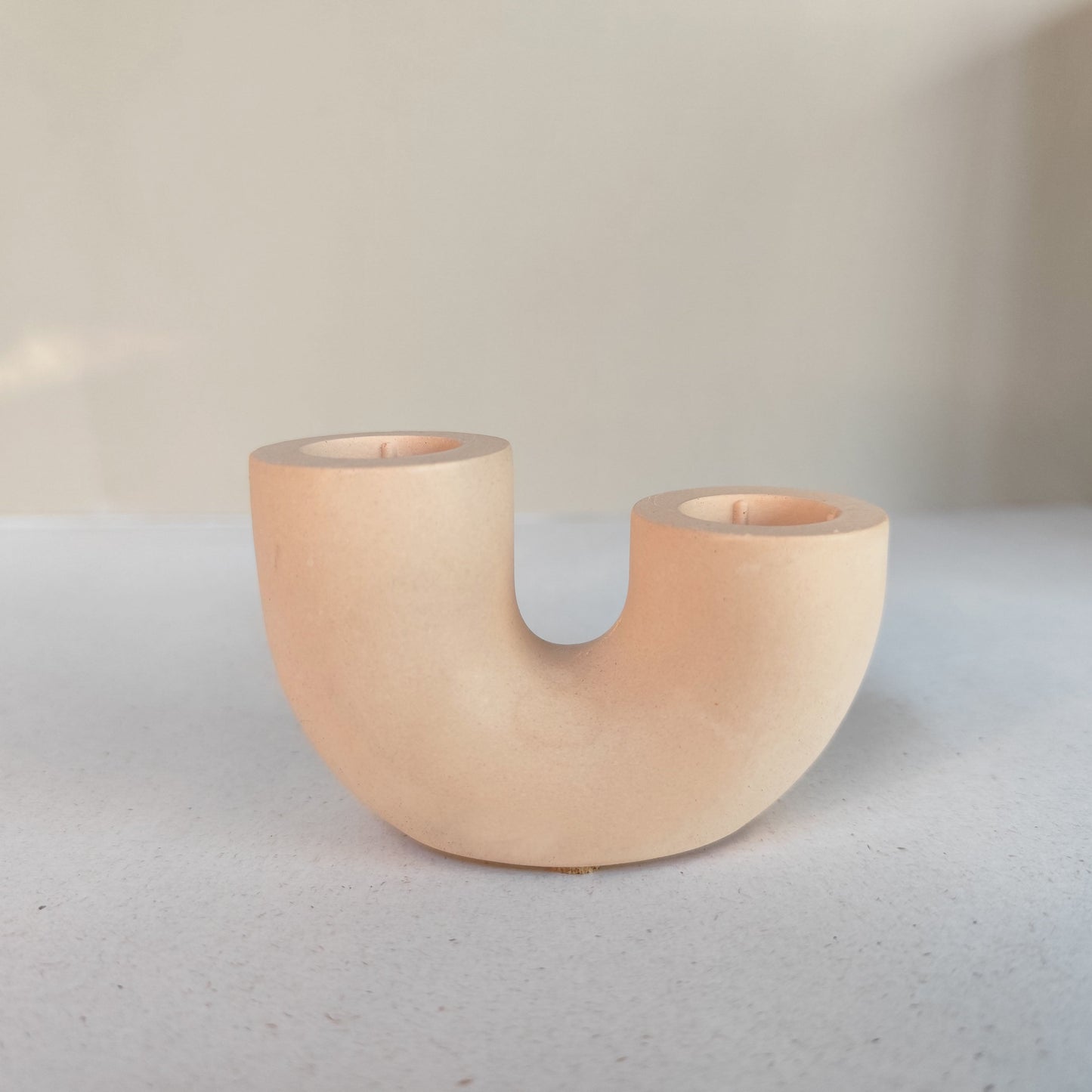 A dual U-shaped candle holder in a nude color, placed on neutral minimalistic  background