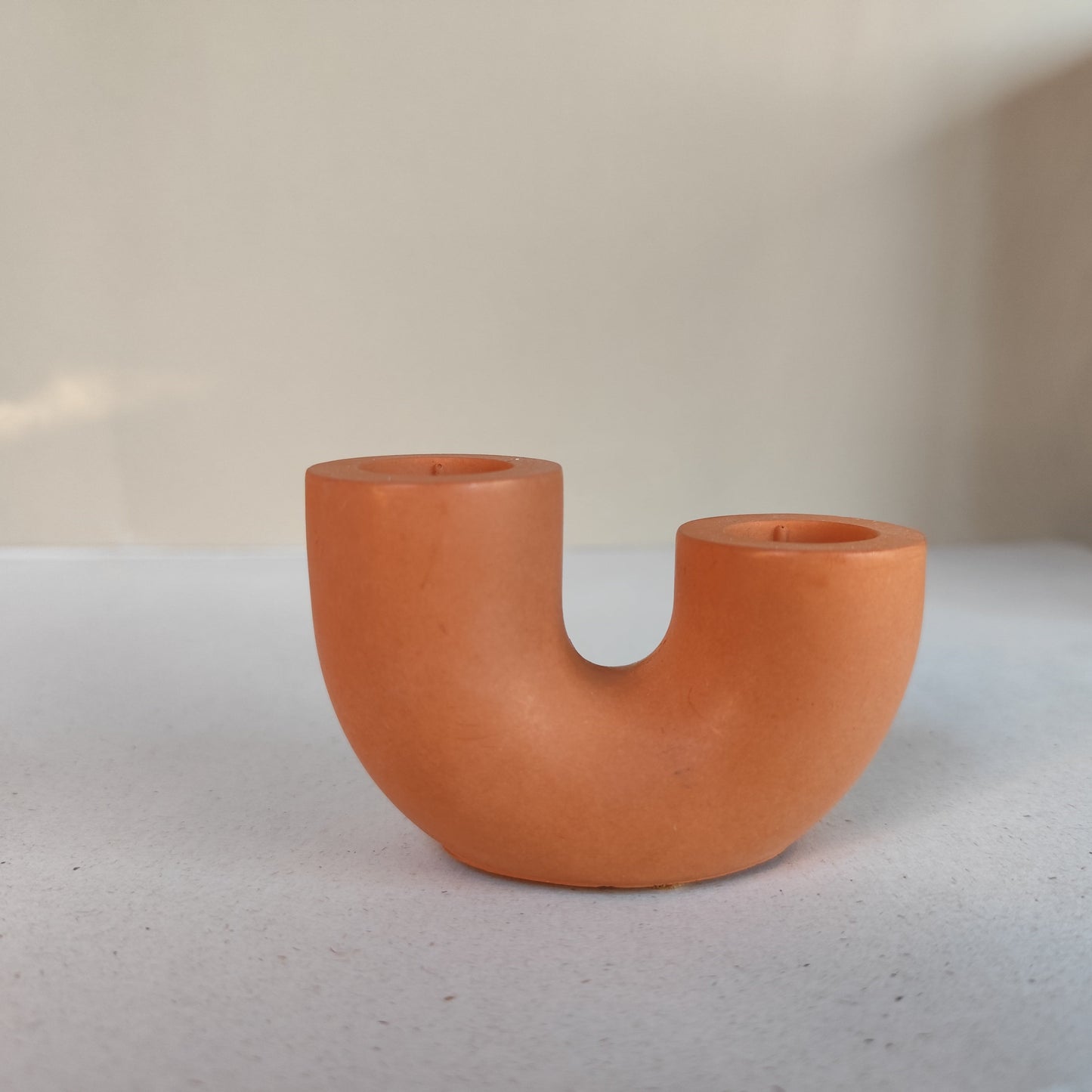 A dual U-shaped candle holder in a terracotta rustic brown colour on a neutral background