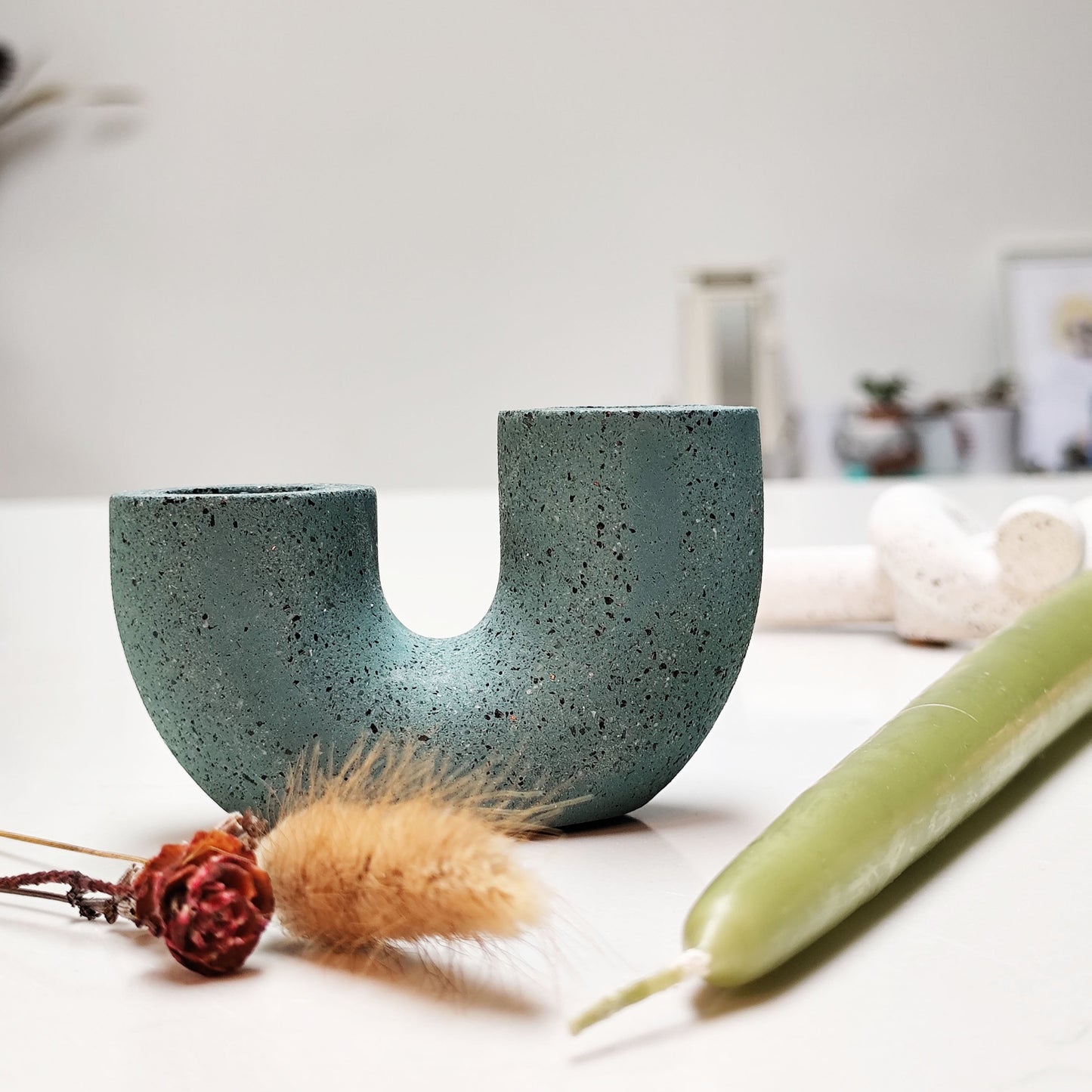 A dual U-shaped candle holder in dark green color, placed on white modern surface with a lime candle beside