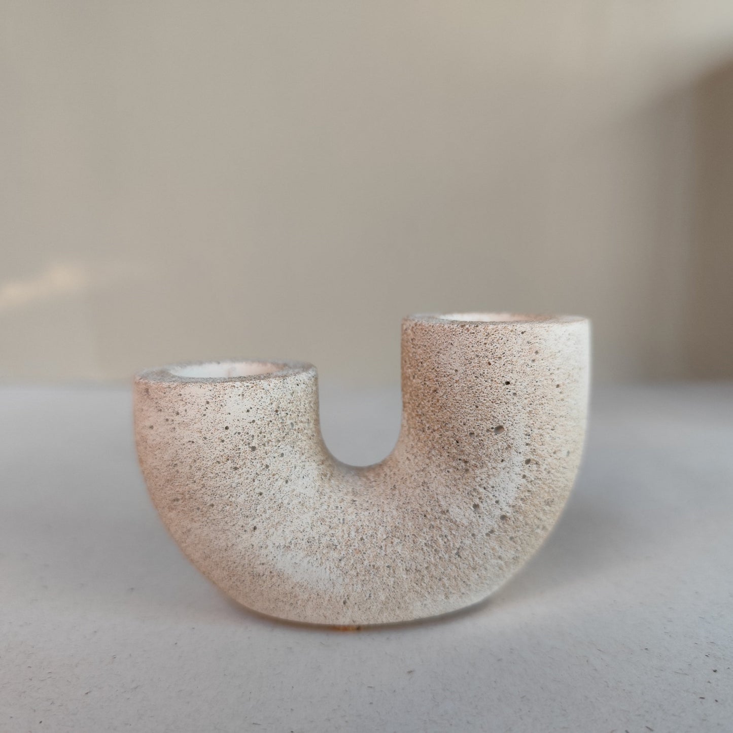 A dual U-shaped candle holder in a beige sandstone color, placed on top of neutral contemporary 