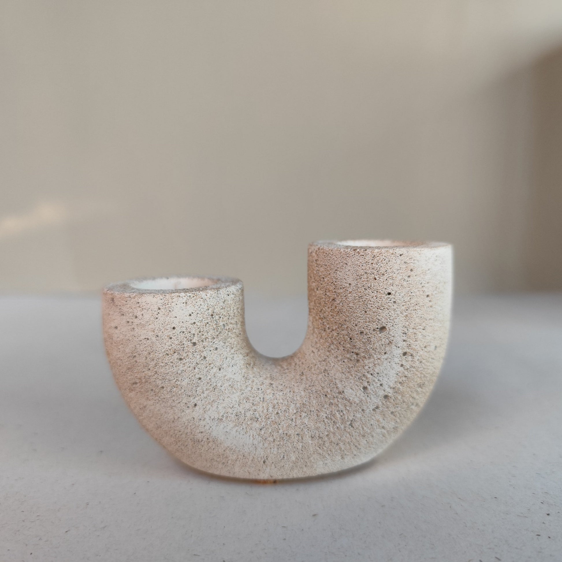 A dual U-shaped candle holder in a beige sandstone color, placed on top of neutral contemporary 