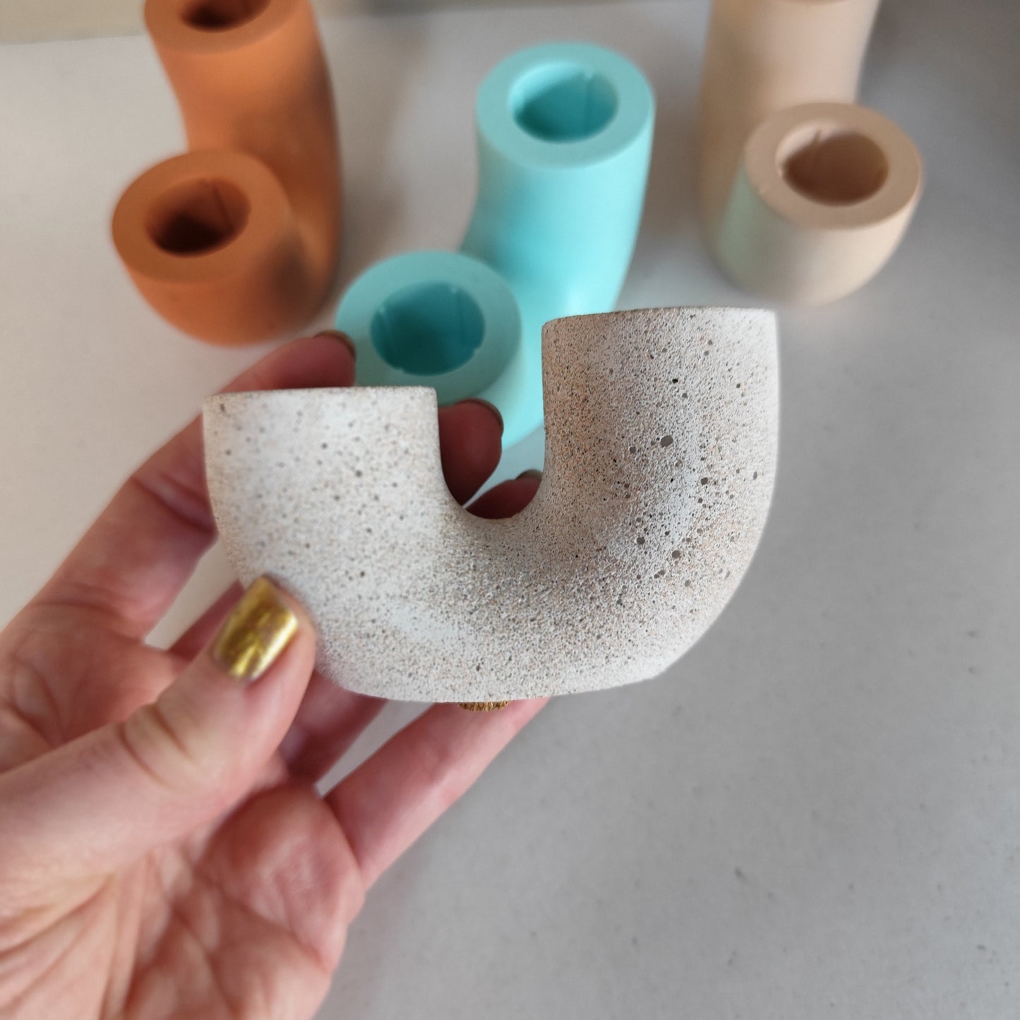 Handcrafted duo candle holder in sandstone picked up to highlight rough texture with mixed colours in the background