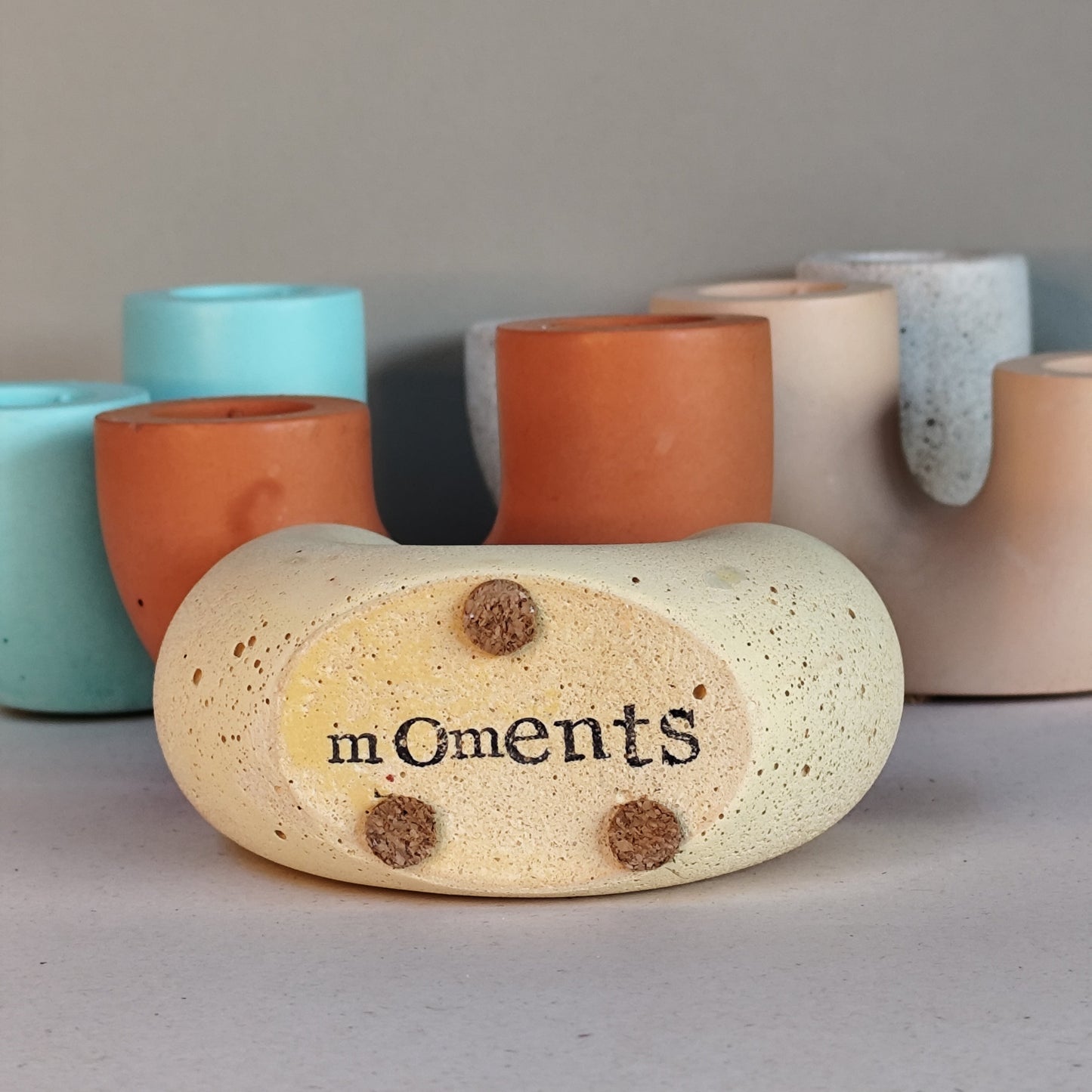 Handmade candle holders in sandstone, terracotta, mint and yellow in a group image with the yellow on side revealing stamped message
