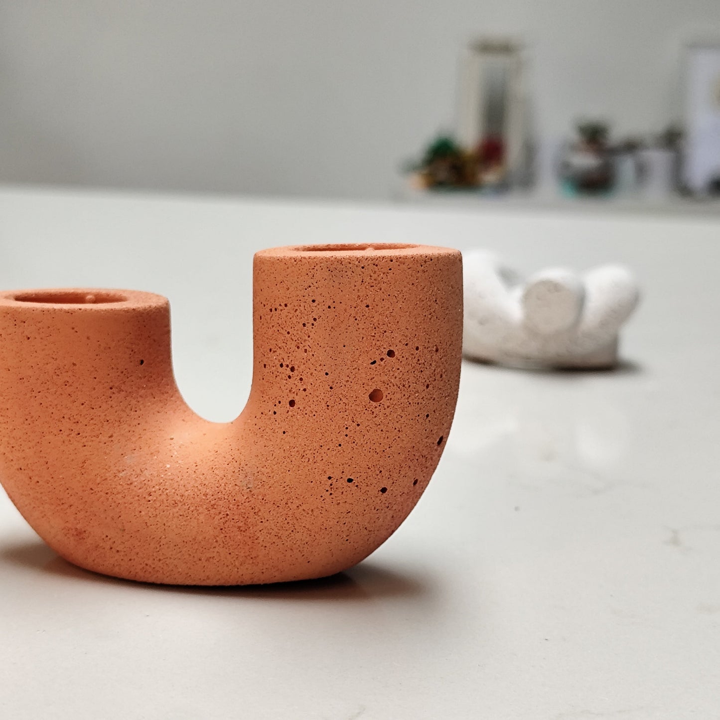 A dual U-shaped candle holder in a orange color, placed on top of white  minimal kitchen