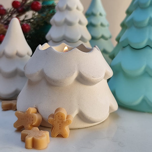 Ceramic Christmas tree-shaped candle holder with a lit candle and gingerbread men on a neutral background.