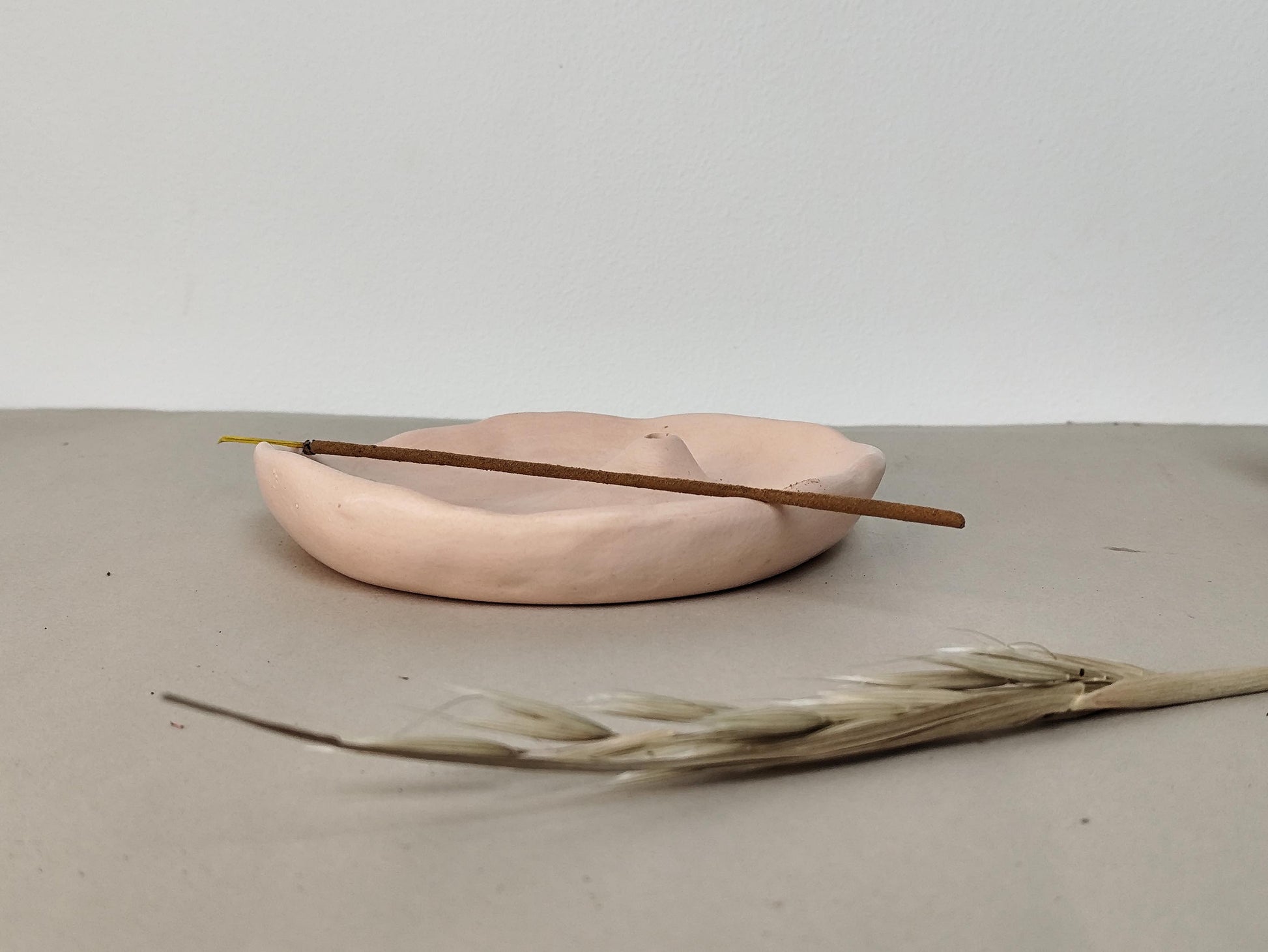 Modern nude jesmonite dish with an incense holder placed delicate on the dishes curves on a gray surface