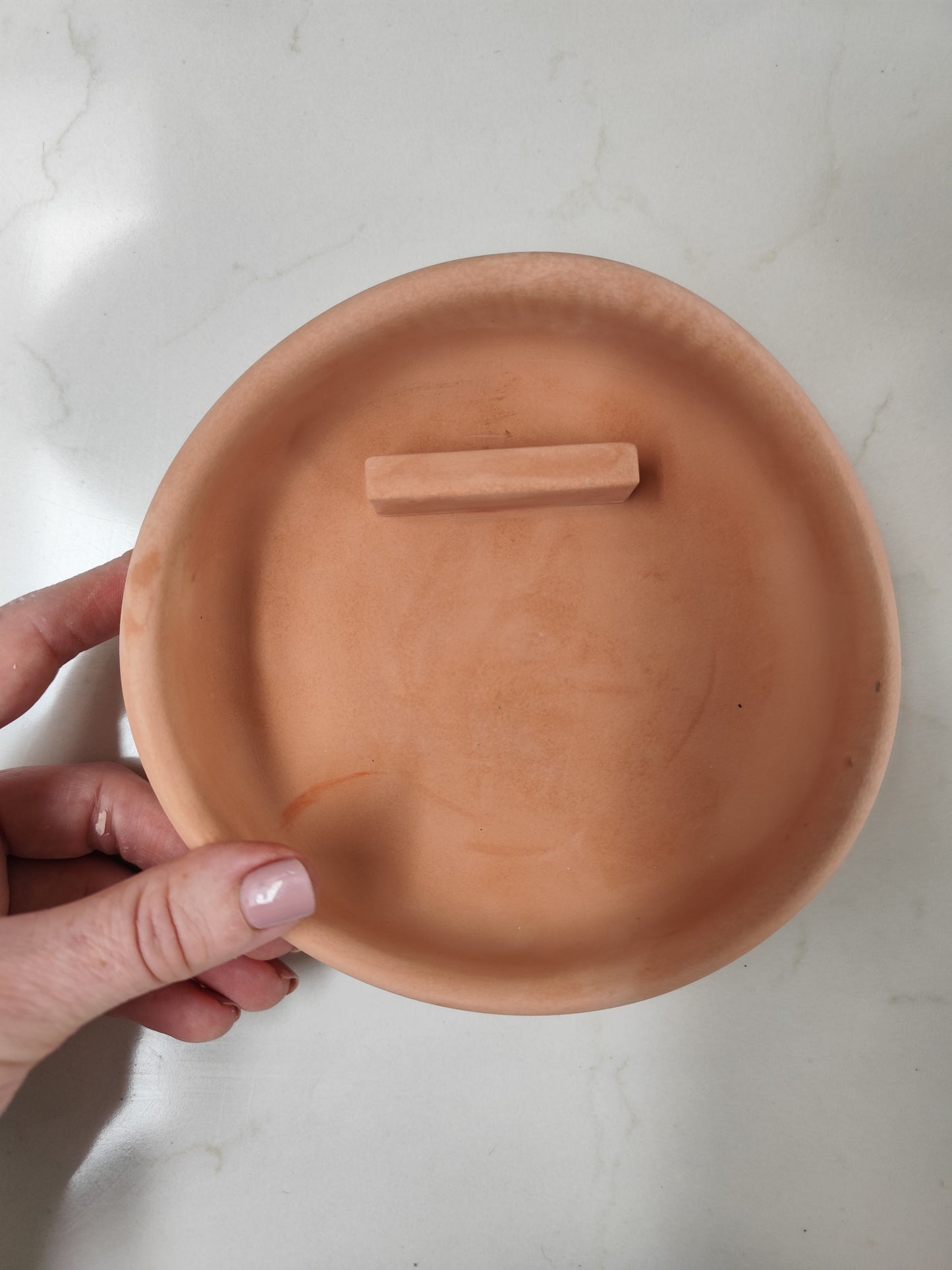 Handcrafted Terracotta Burner with the side held by a hand on a light background