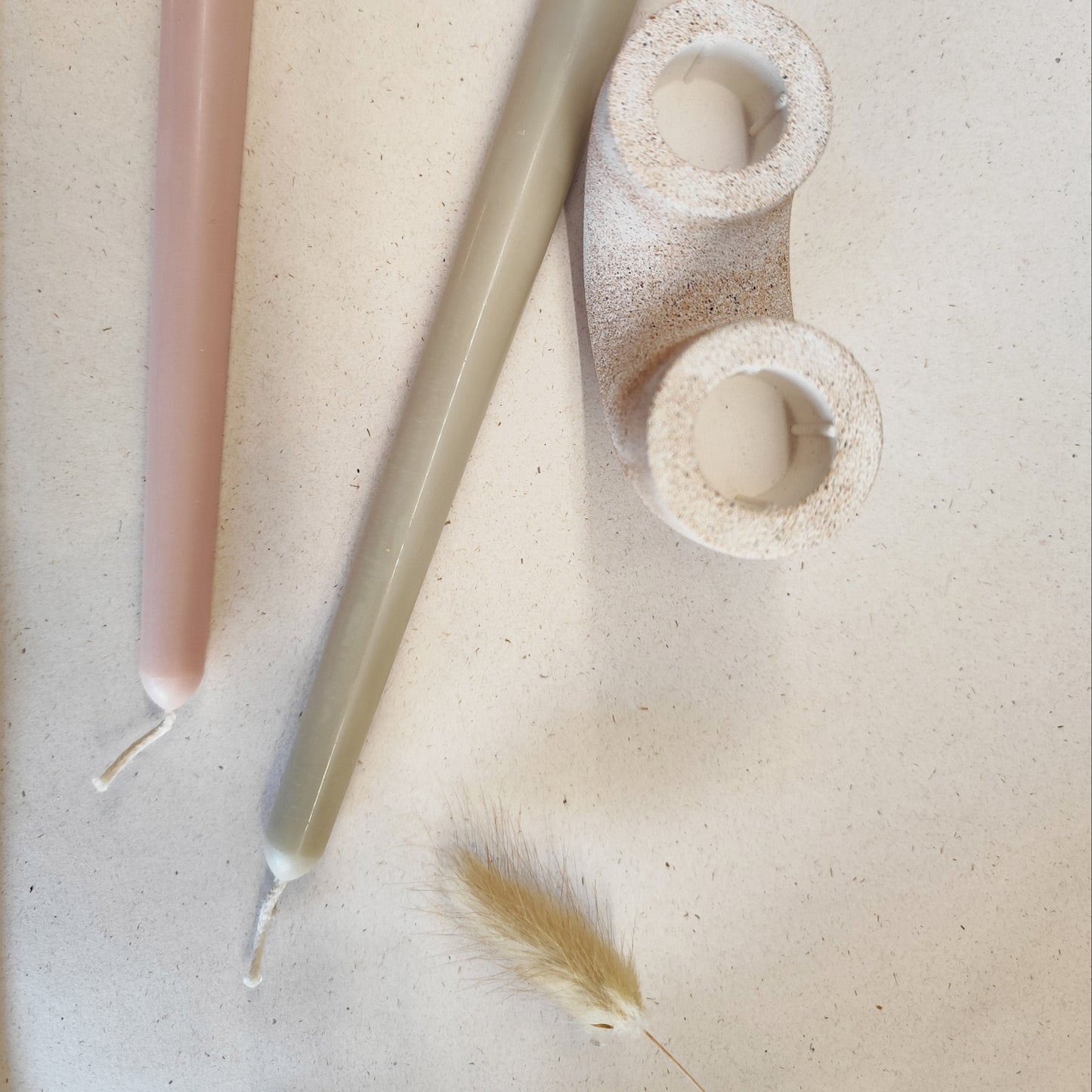 overhead close up view of the beeswax taper candles colours nude and sage alongside a sand duo candle holder