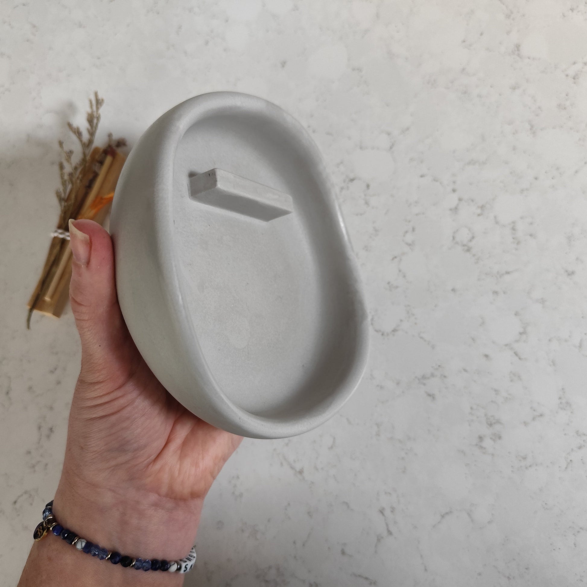 Hand holding aside of burner showing a handcrafted wave curve textured surface against a light gray background