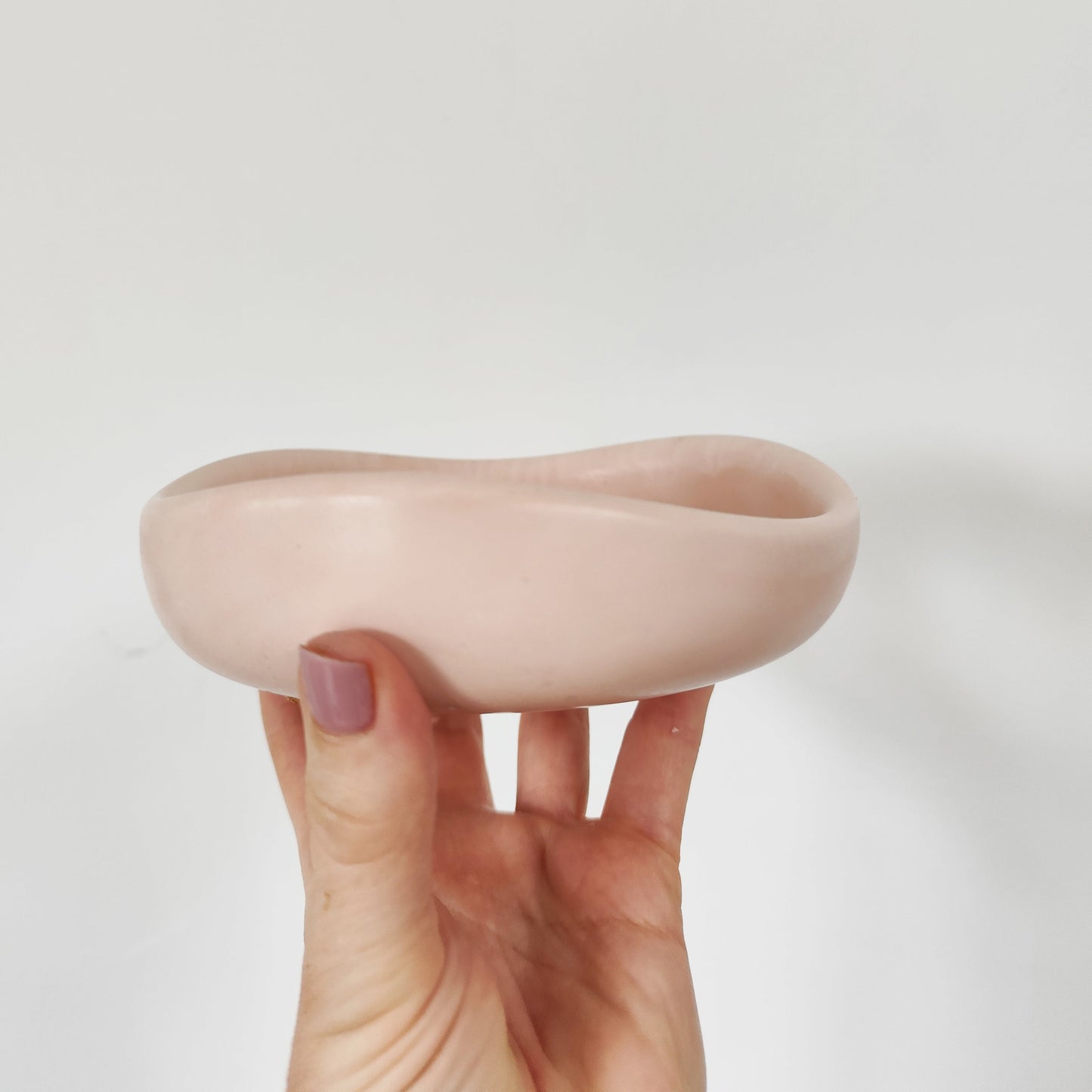 Hand holding a pink jesmonite palo santio bowl against a white background showcasing the side view