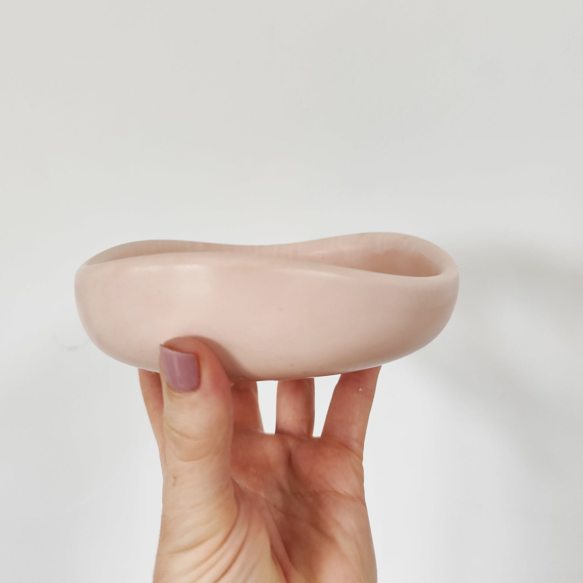 Hand holding a pink jesmonite palo santio bowl against a white background showcasing the side view