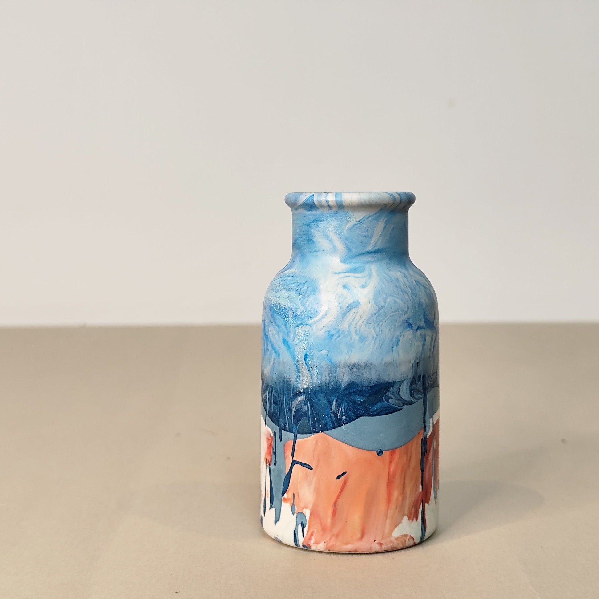Vase with blue and pink marbled design on a beige surface and light gray background