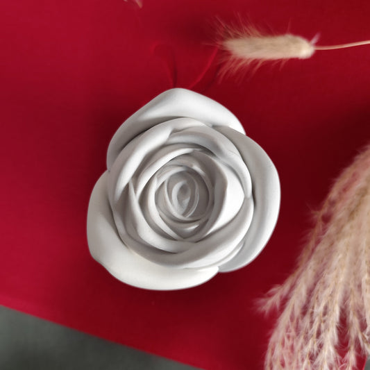 A close-up image of a pink rose-shaped candle placed on a red surface, with a wooden wick visible and surrounded by dried plants.