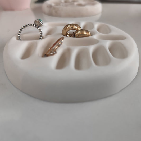 White ring dish holding two rings and a pair of earrings