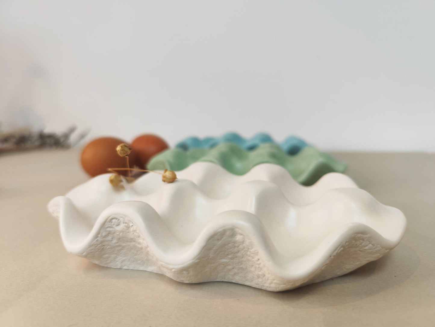 White jesmonite smooth shaped egg storage tray with dried plant on top.