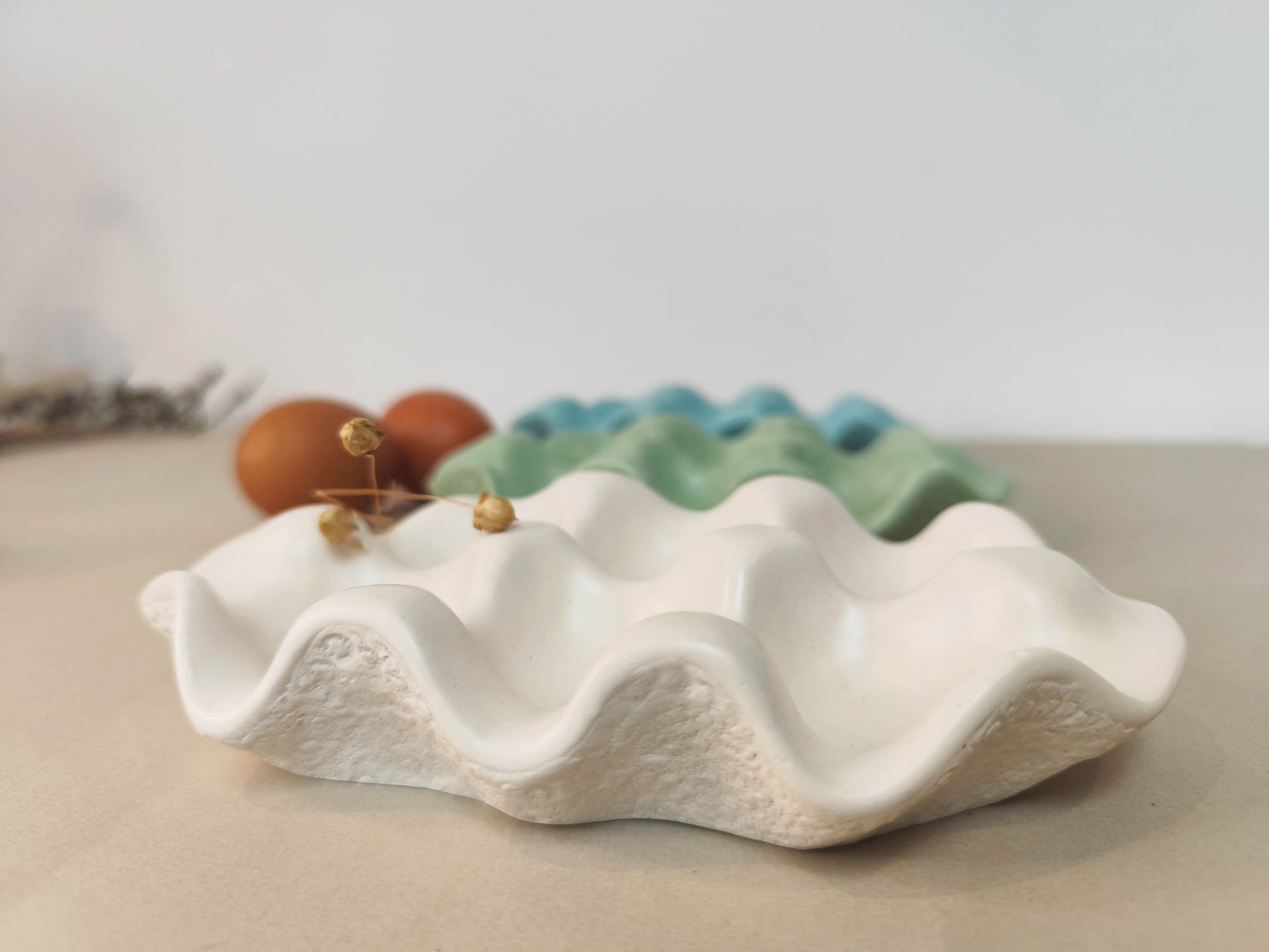 White jesmonite smooth shaped egg storage tray with dried plant on top.