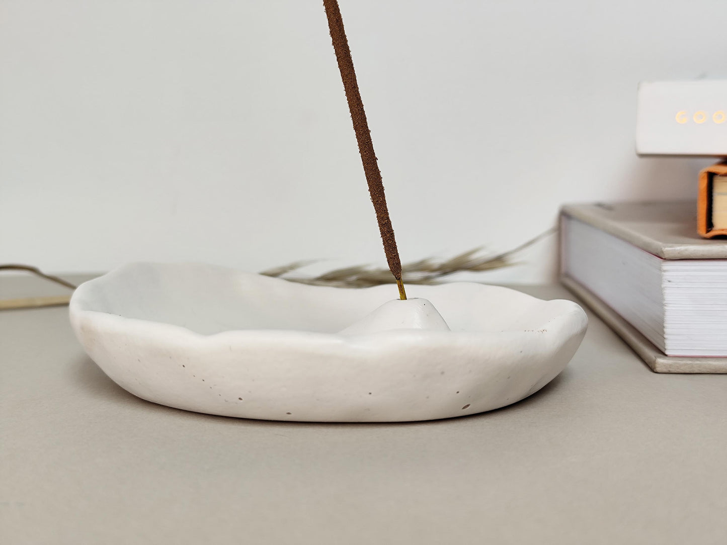 Incense stick burning in a white minimal jesmonite dish on a light surface.