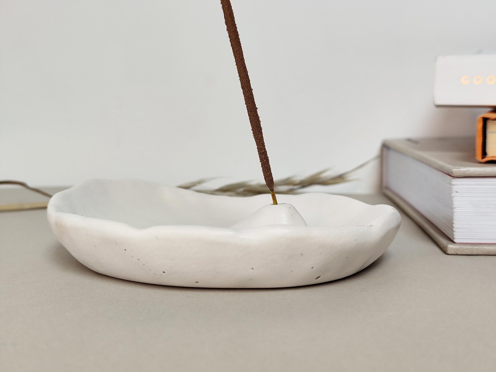 Incense stick burning in a white minimal jesmonite dish on a light surface.