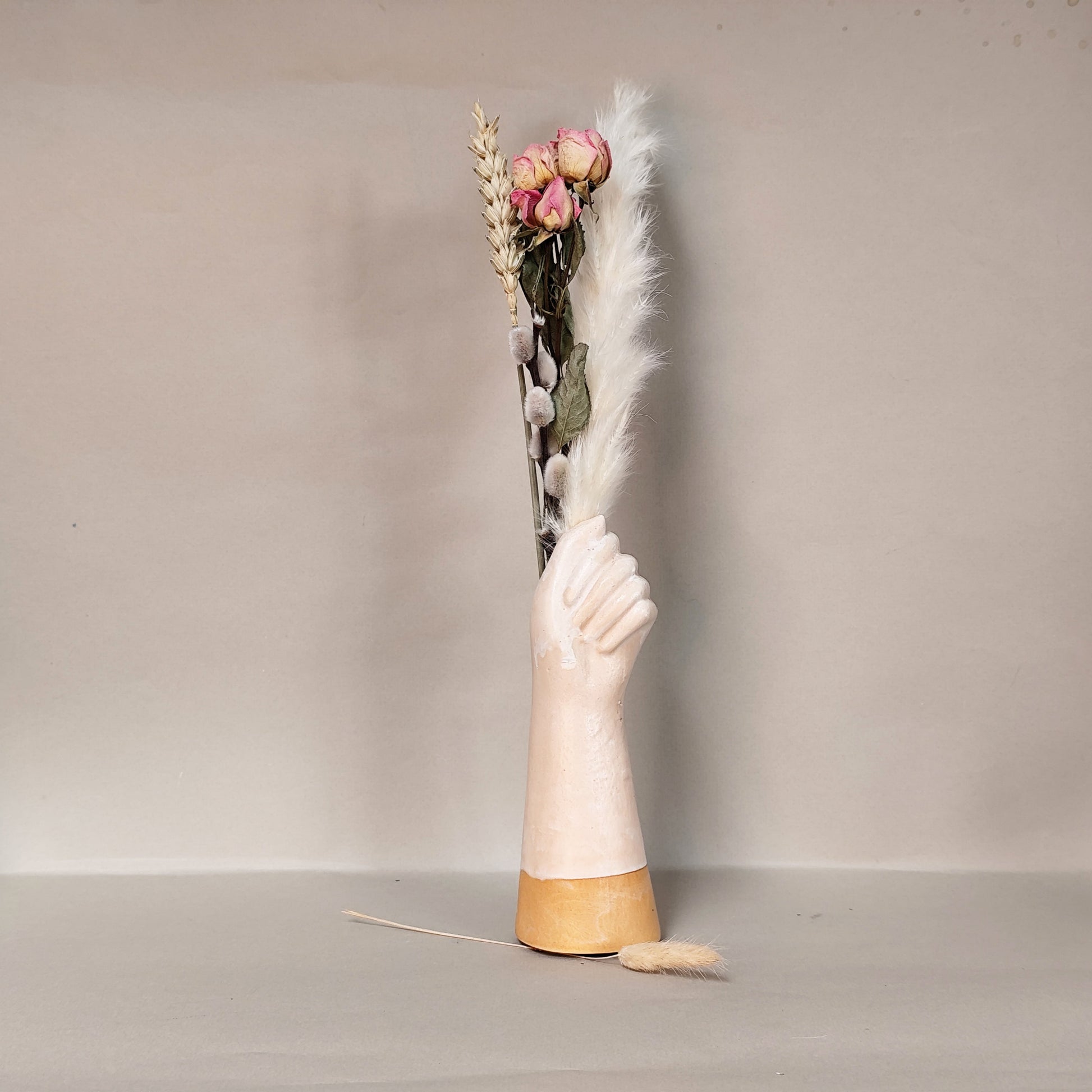 Vase shaped like a hand with dried flowers on a neutral background