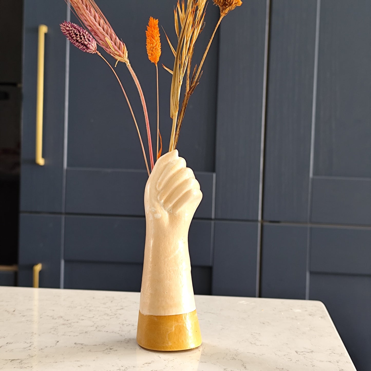 Vase shaped like a hand with dried flowers on a marble kitchen island