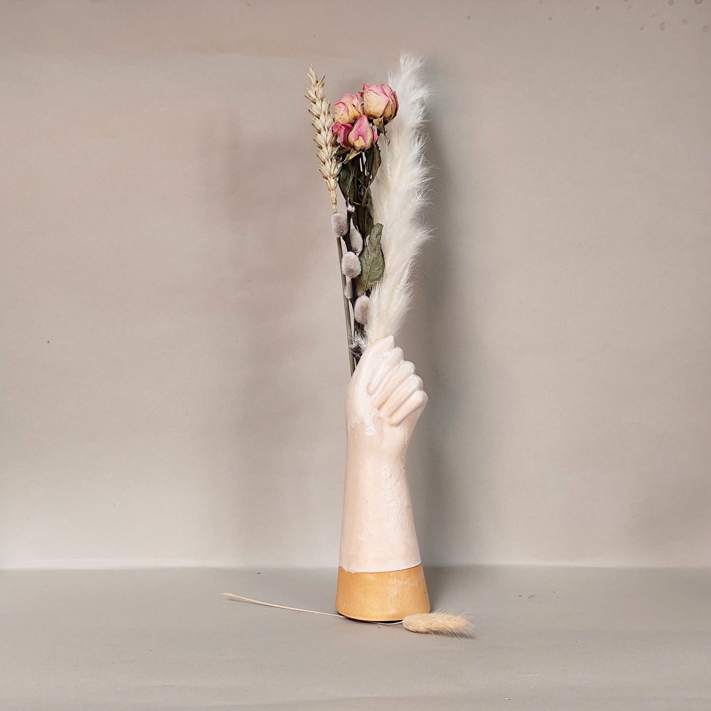 Handmade Vase shaped like a hand with closed fist holds dried flowers on a neutral background