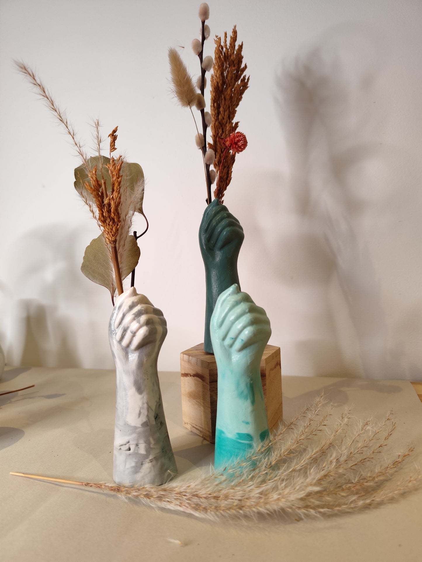 Three hand-shaped vases with dried plants on a neutral background