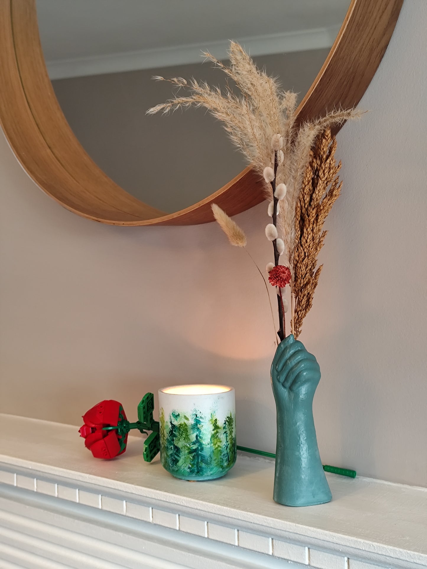 Decorative items including a hand-shaped vase with dried plants, a candle, and a small rose on a shelf.