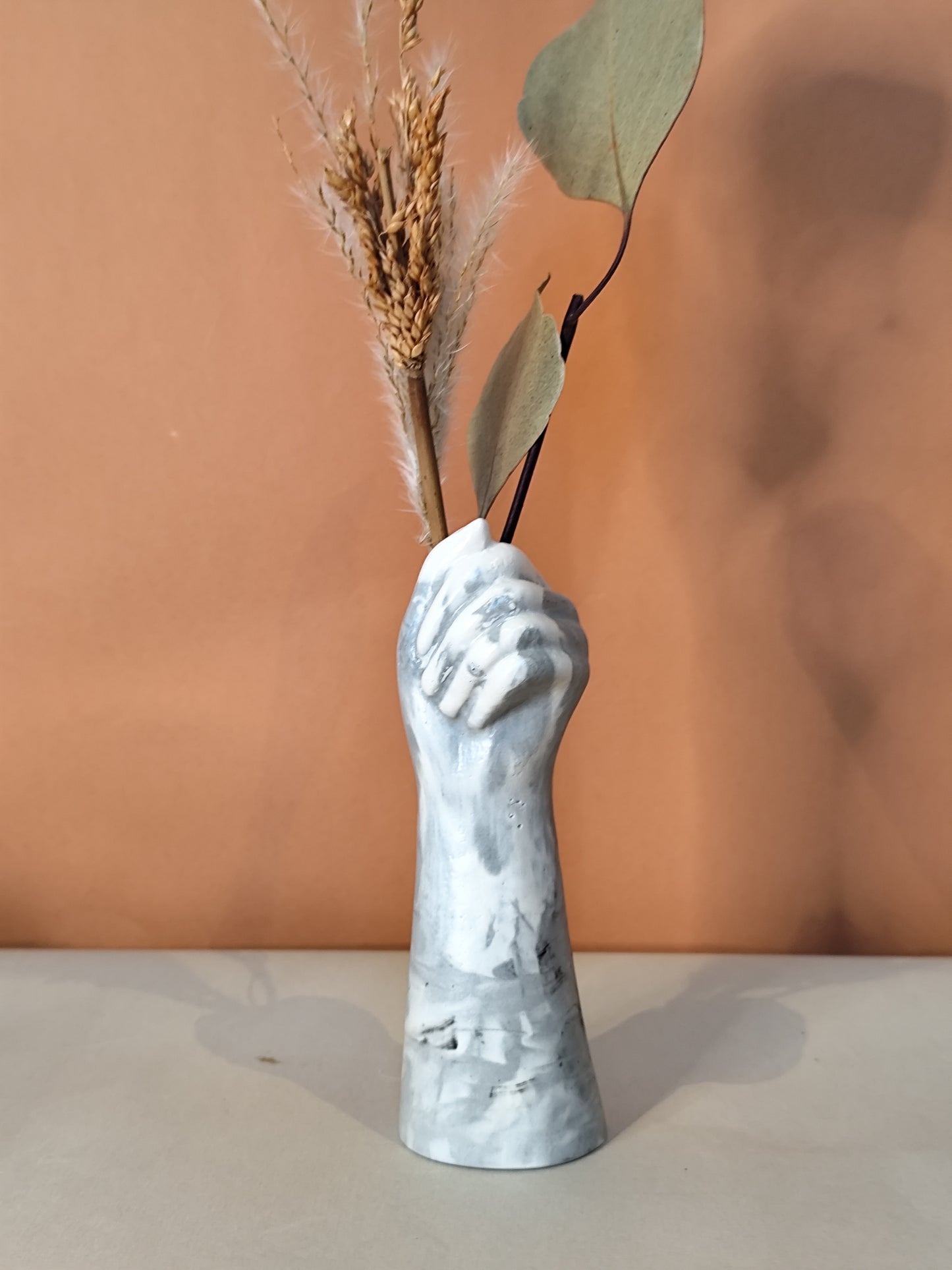 Handcrafted Vase shaped like a hand holding dried plants against a brown background