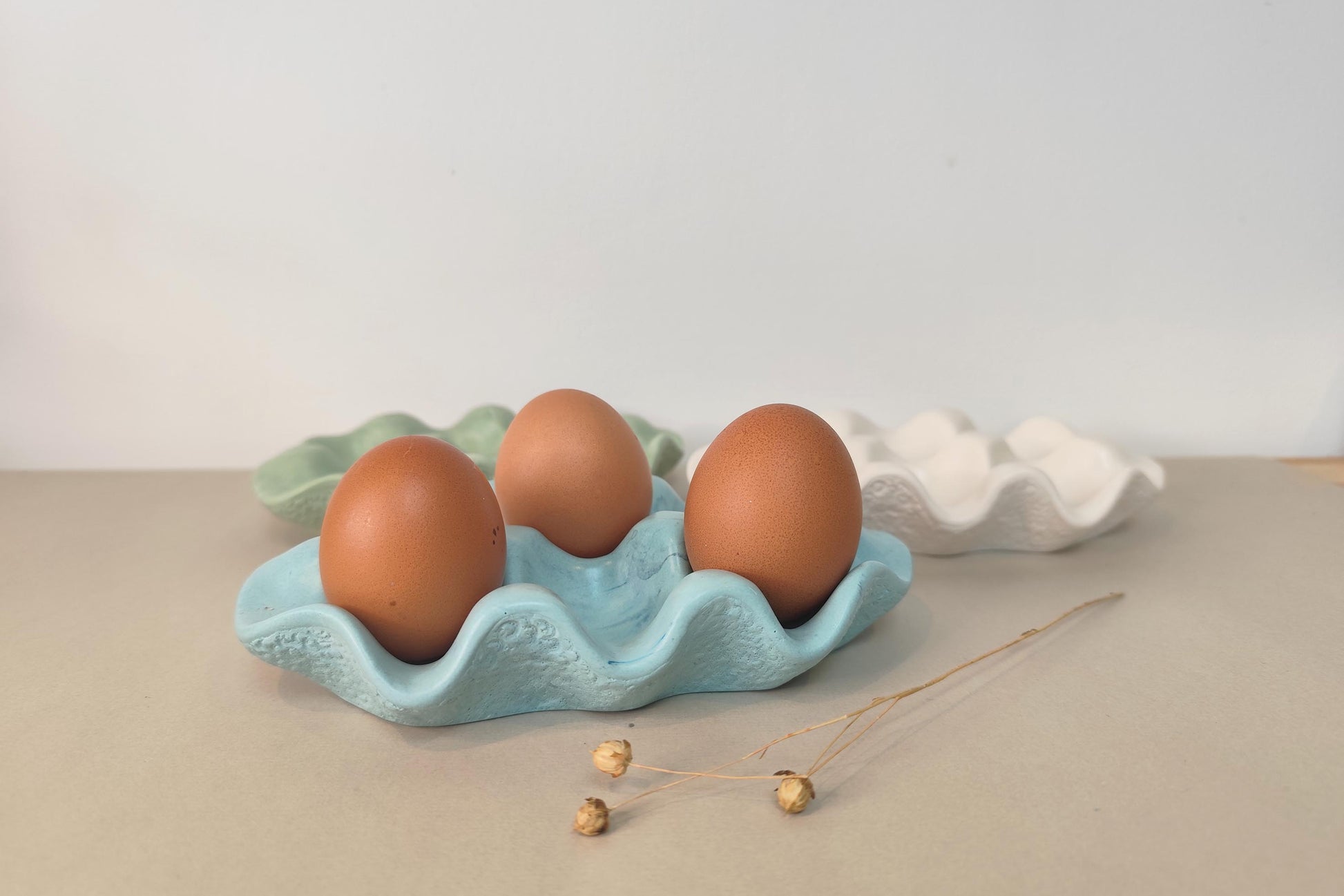Three brown eggs in a light blue jesmonite egg holder on a beige surface with a white background.