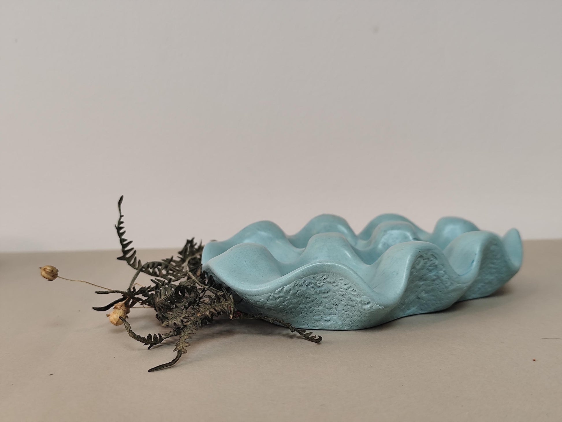 Blue jesmonite smooth shaped egg tray with dried plant on a beige surface