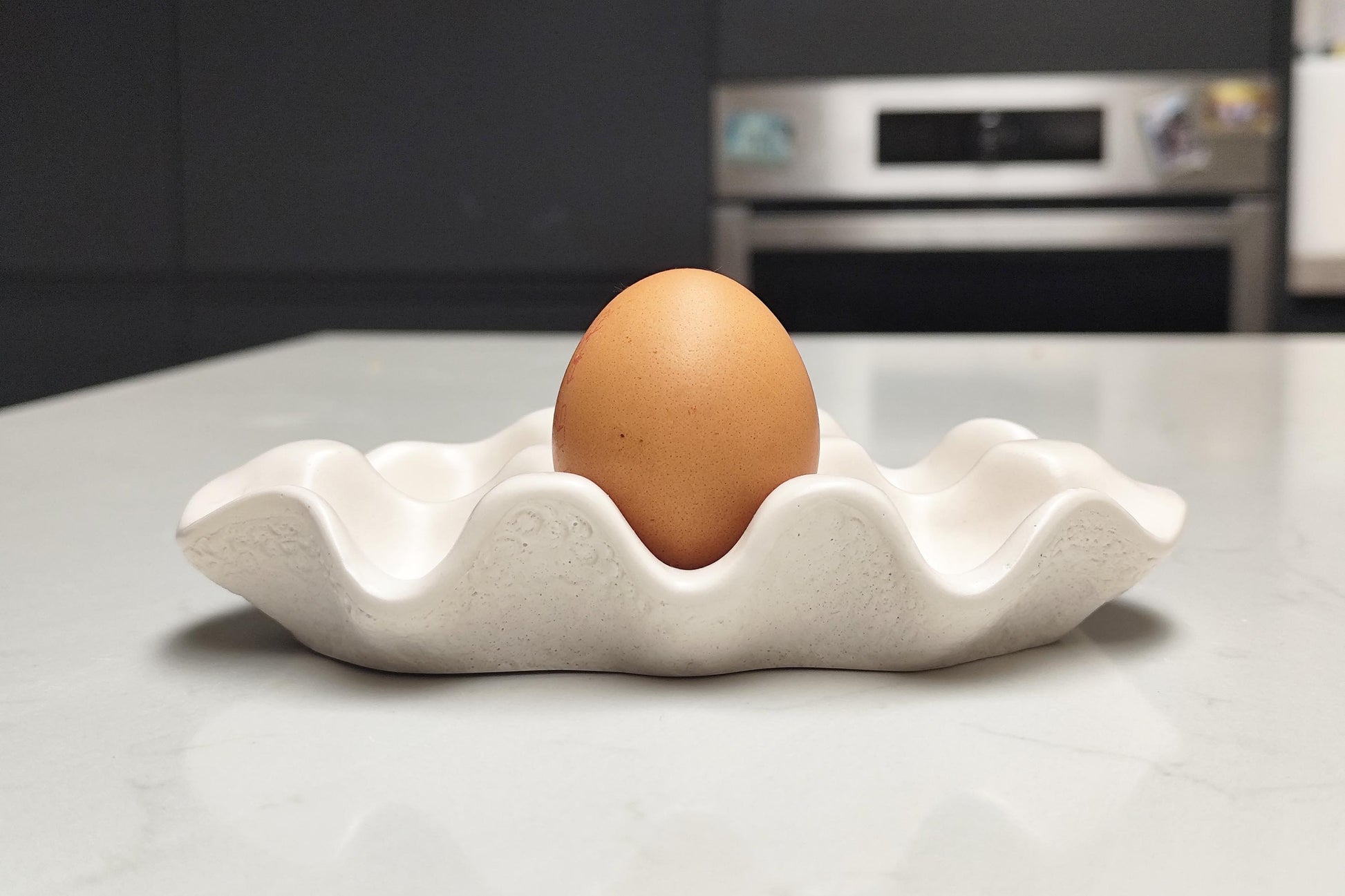 Brown egg in a white handmade jesmonite egg holder on a kitchen counter
