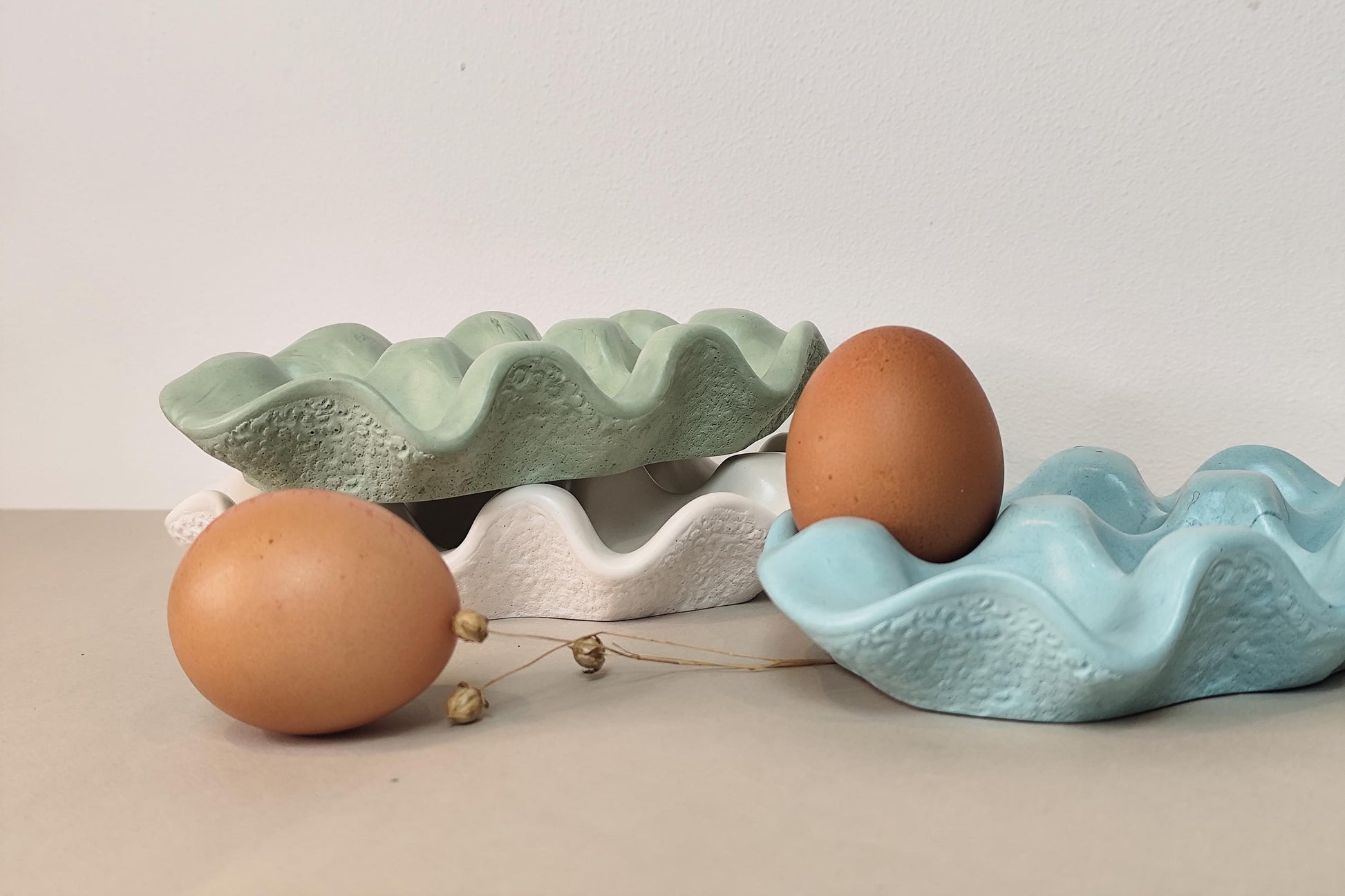Two jesmonite egg trays, one green and one blue, with two brown eggs on a neutral background.