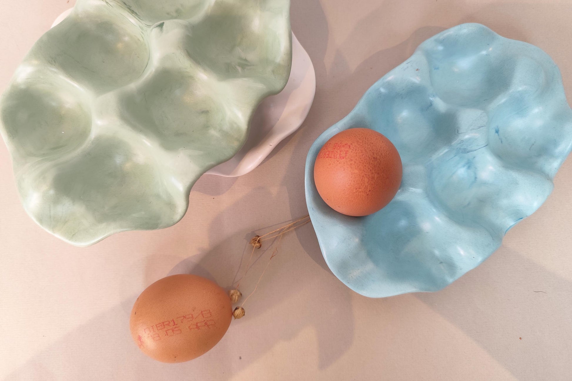 Two jesmonite egg trays, one green and one blue, with eggs on a pink surface, overhead view