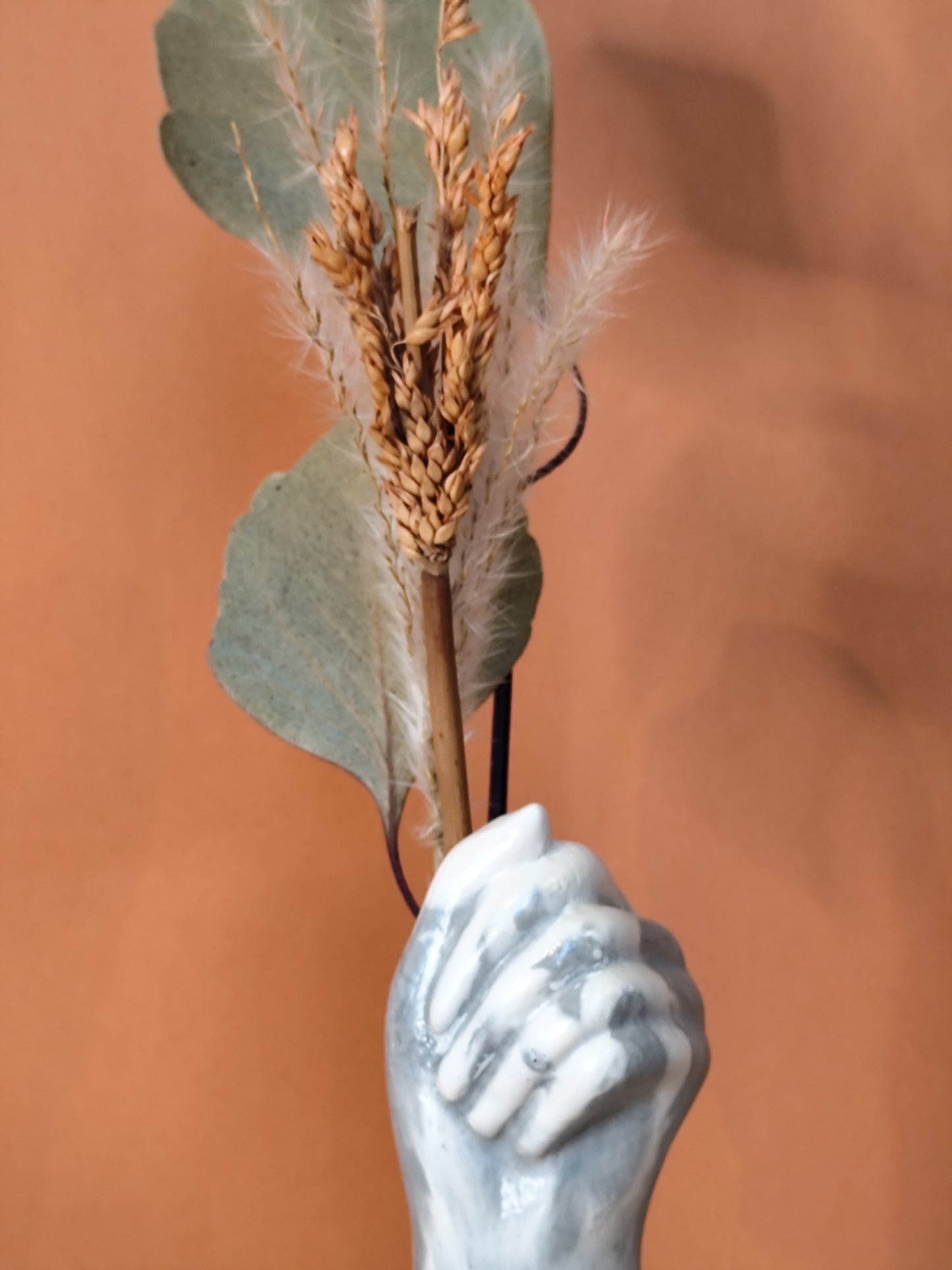 Close up of hand vase with dried flowers against a brown background