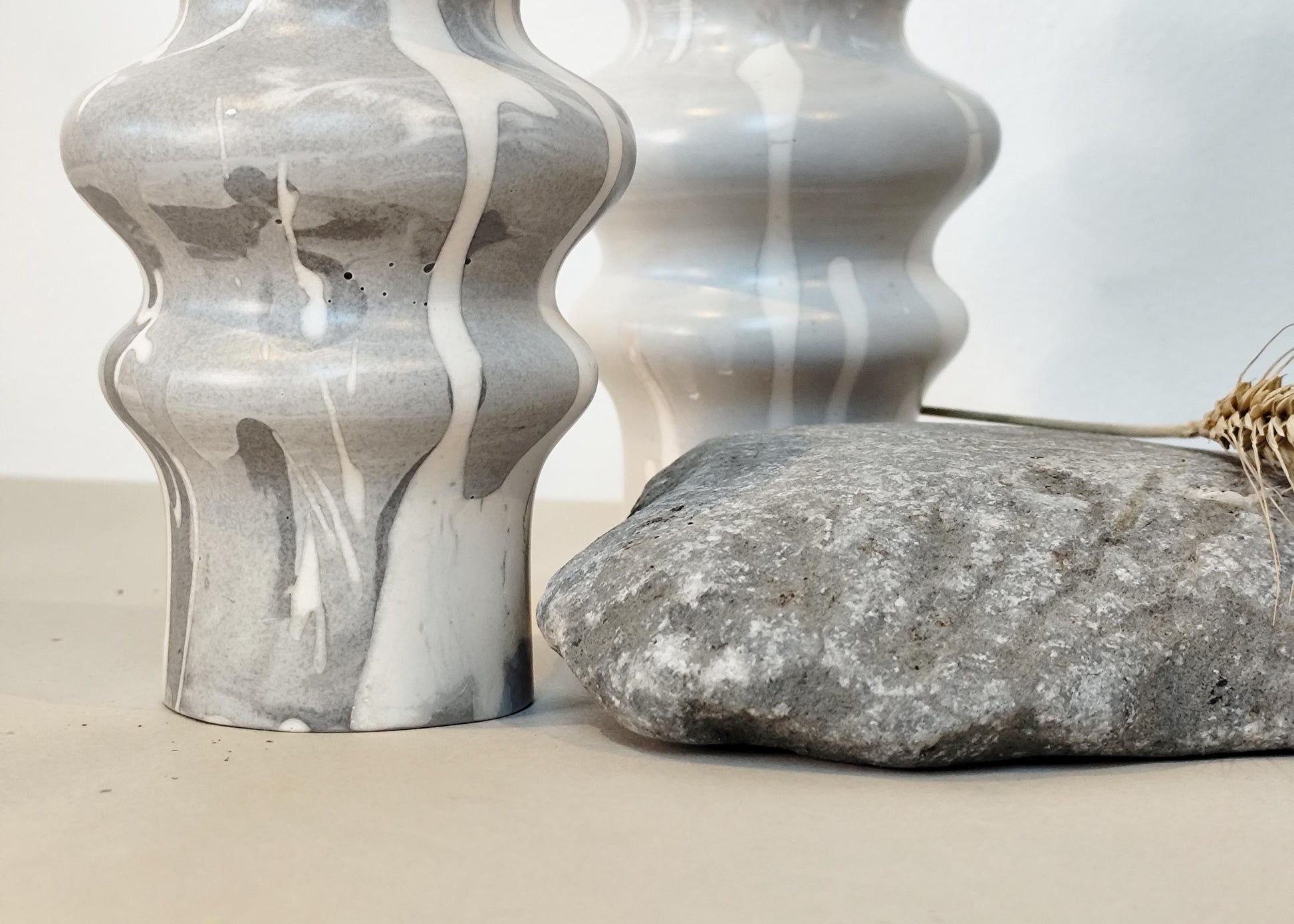 Two gray textured vases and a large stone on a light background