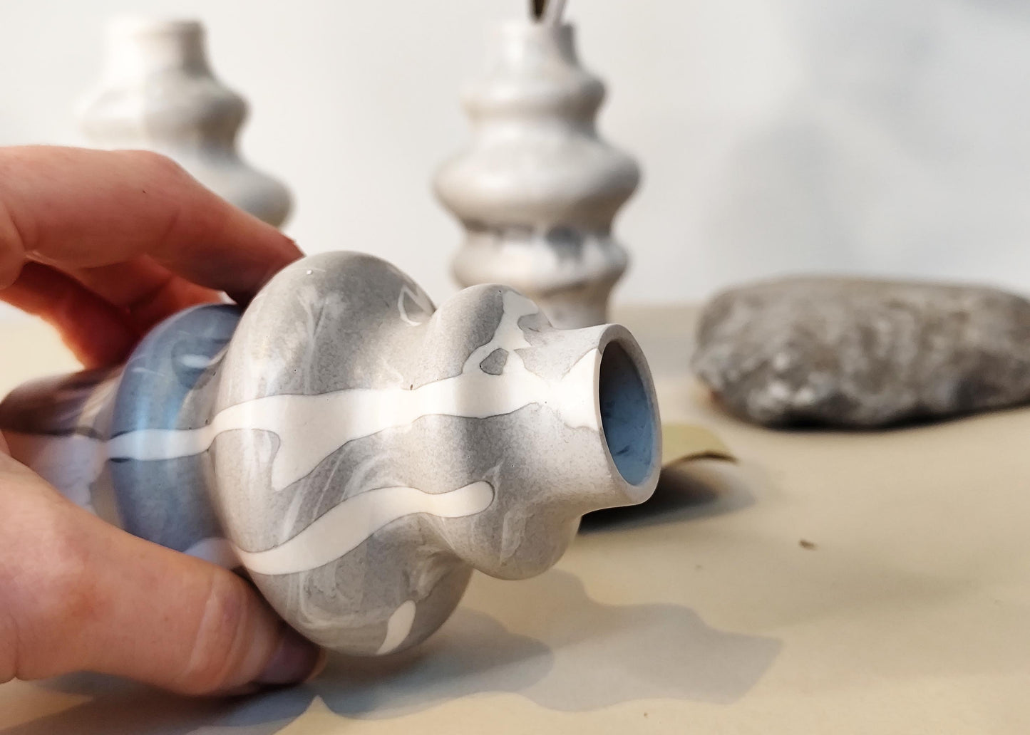 Hand holding a small marbleized jesmonite vase with more vases in the background.