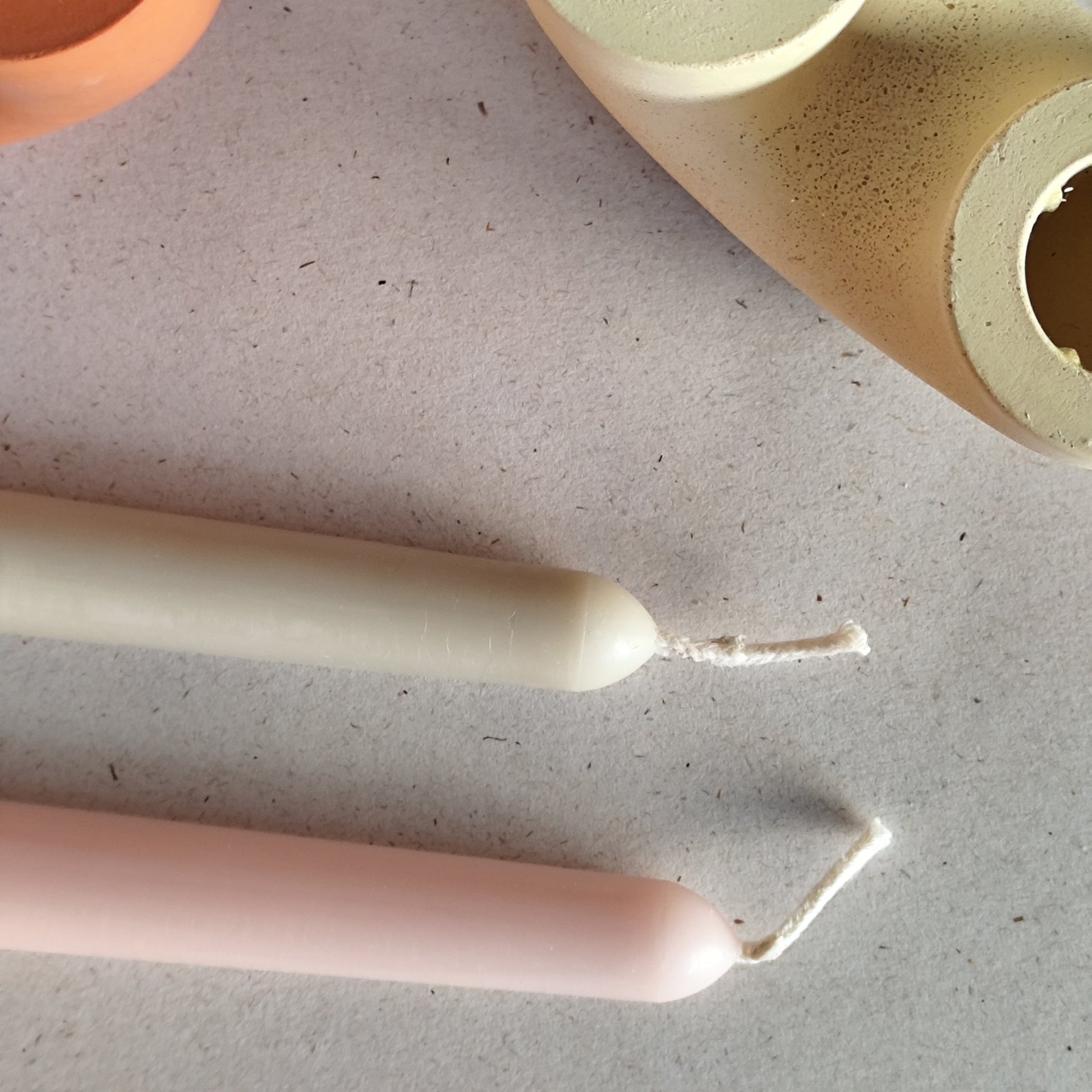 overview photo of yellow candle holder and two beeswax candles lying beside it on white background candles are light green and light pink