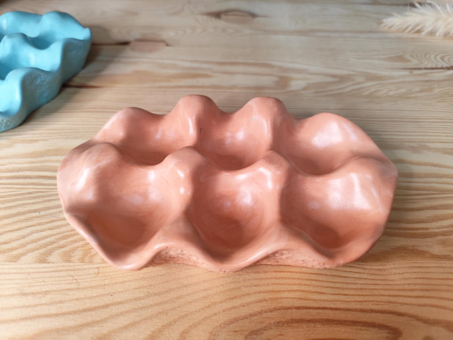 Rustic orange/brown jesmonite smooth shaped egg tray with dried plant on a beige surface