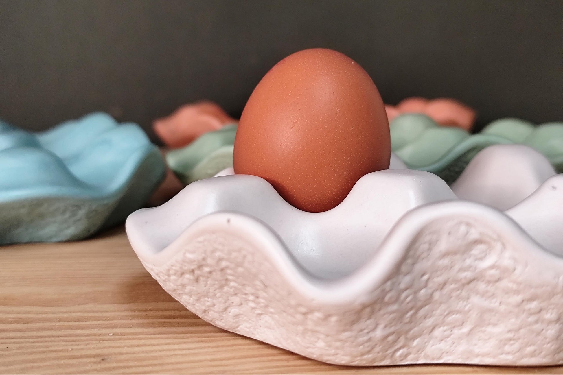 Brown egg in a white jesmonite egg holder on a wooden kitchen surface