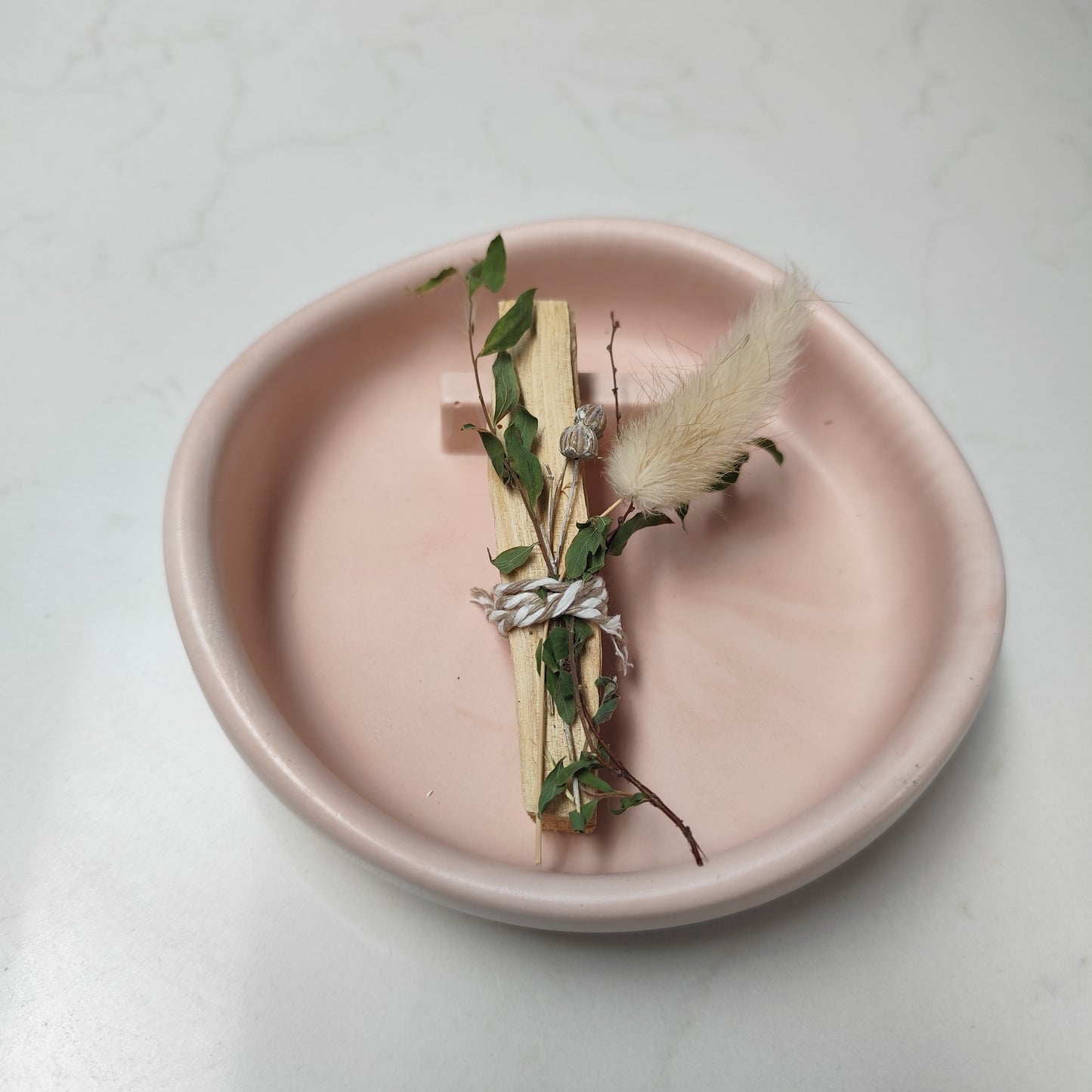 Decorative arrangement of dried flowers on a palo santo stick on a nude jesmonite Burner with a light background