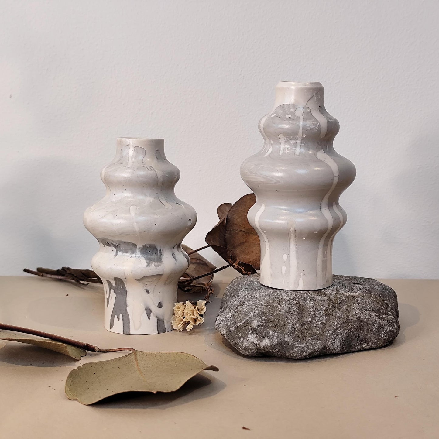 Two hand crafted jesmonite vases on a rock surface with a neutral background
