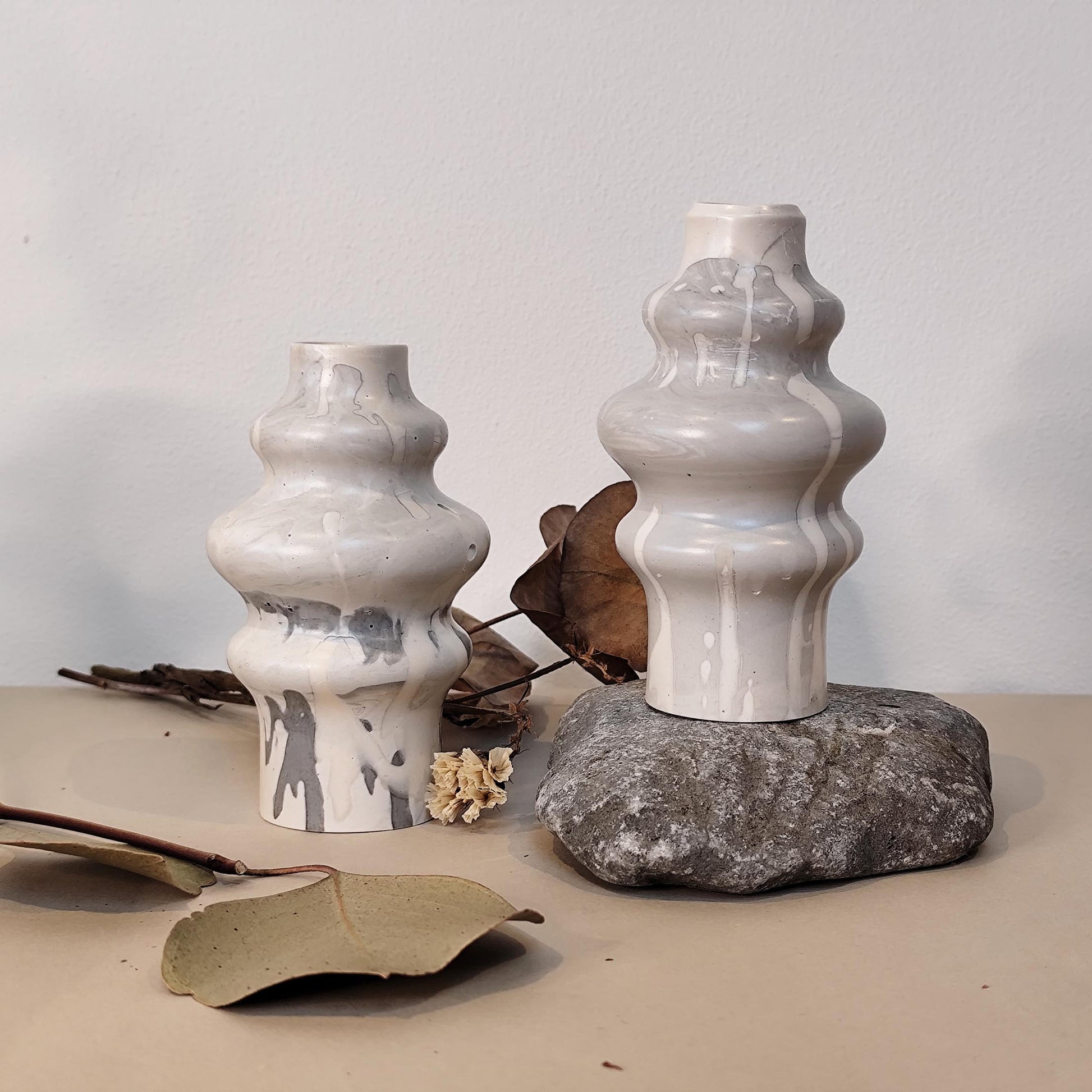 Two hand crafted jesmonite vases on a rock surface with a neutral background