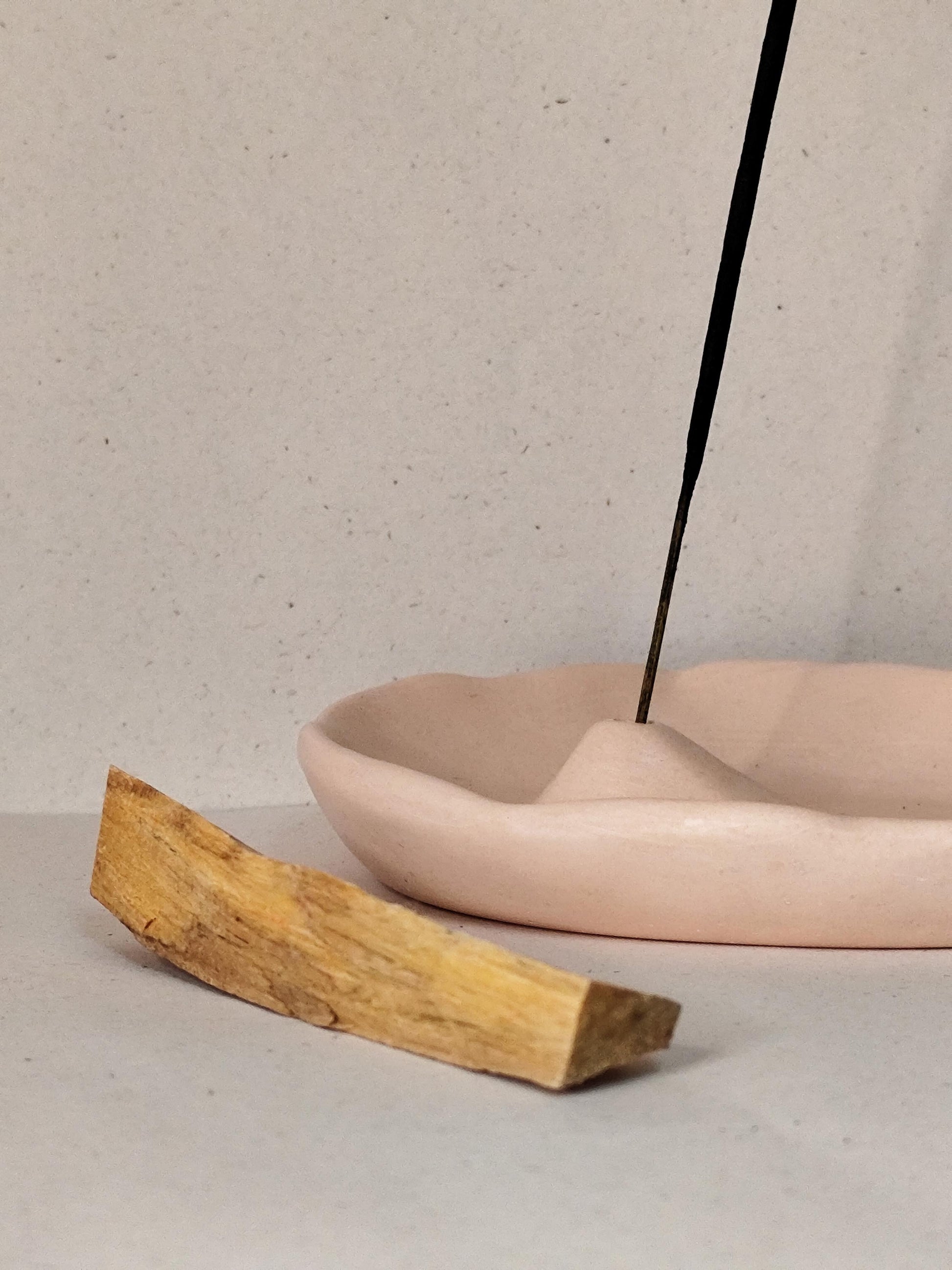 Incense stick burning in a modern nude holder with a wooden block on a neutral background